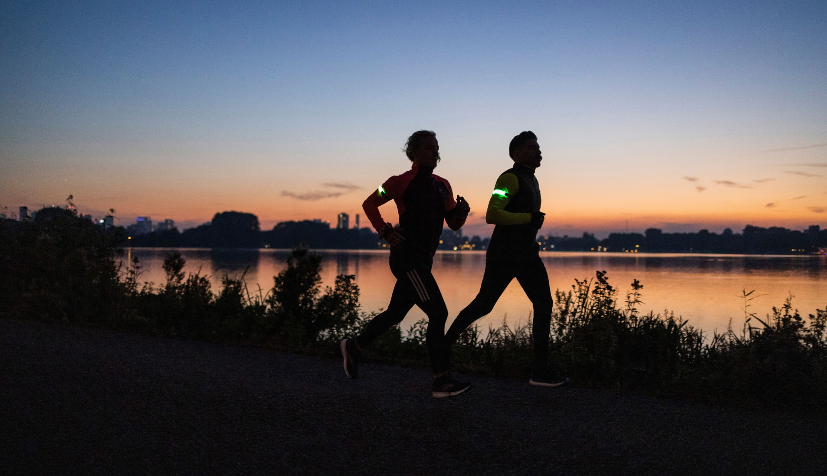 Twee hardlopers rennen langs het water in de schemer met reflecterende accessoires