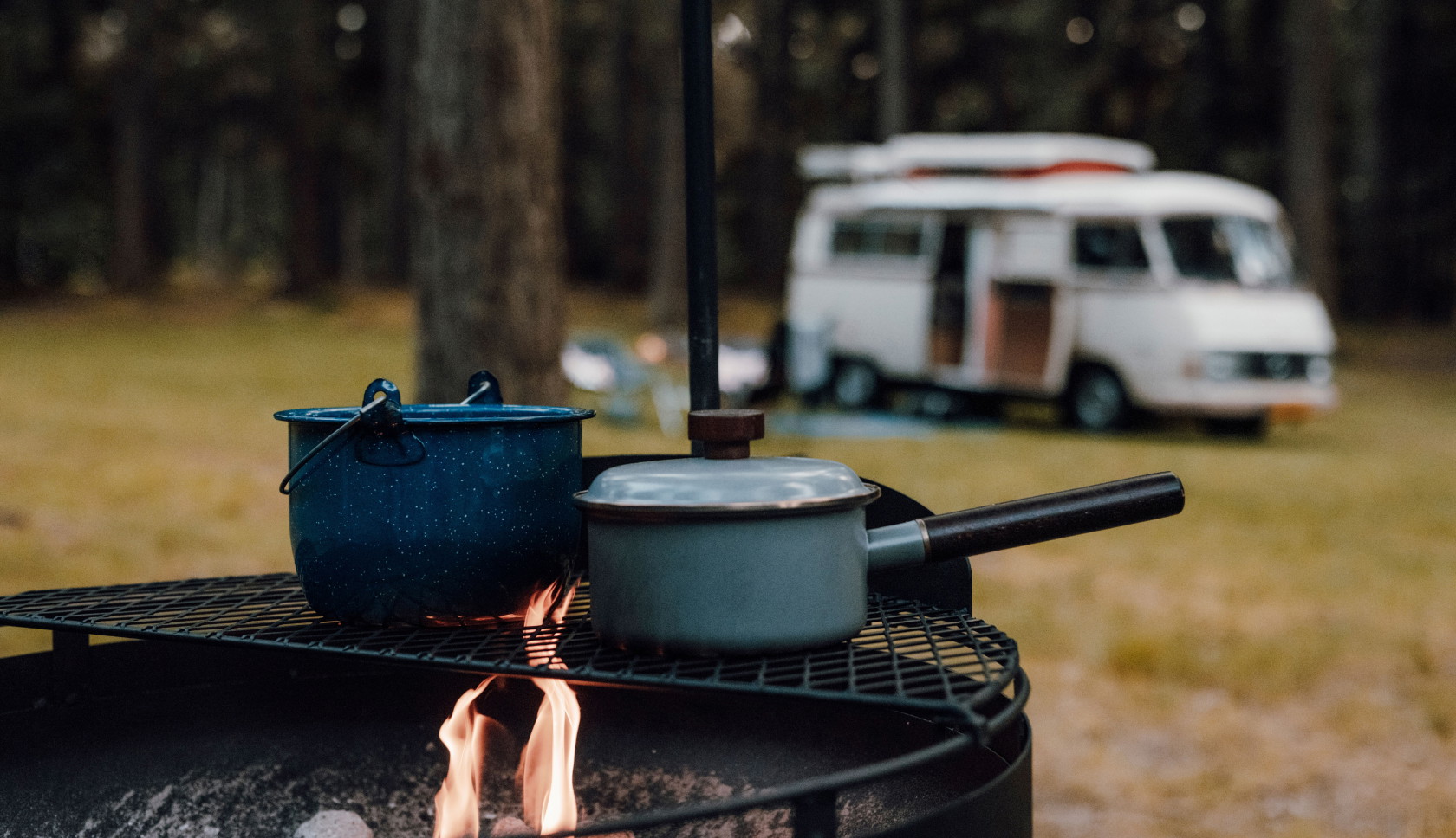 Twee pannetjes staan op een vuur met op de achtergrond een camper