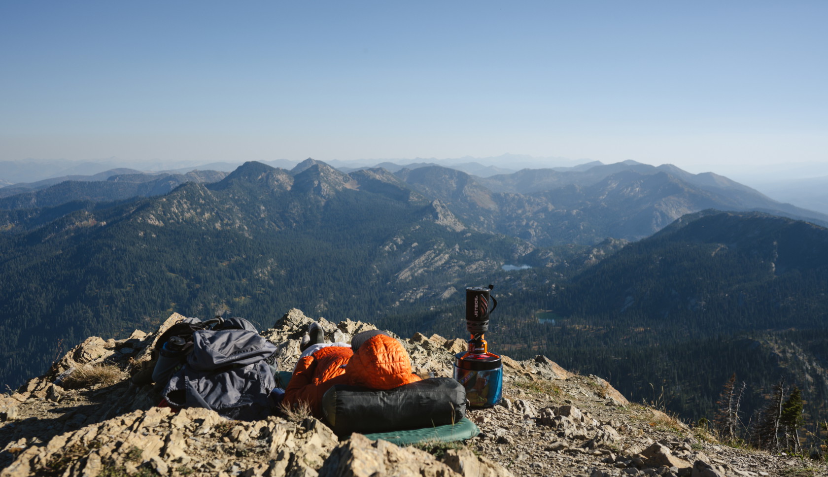 Een persoon ligt op een slaapzak op de grond en kijkt uit over talloze bergtoppen