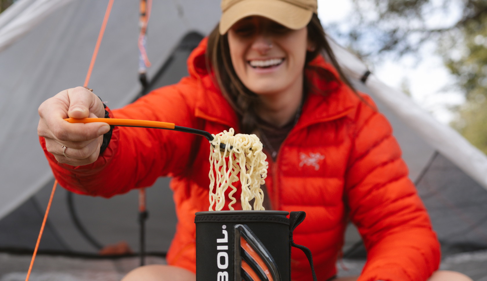 Een lachende vrouw schept noedels uit een Jetboil-brander