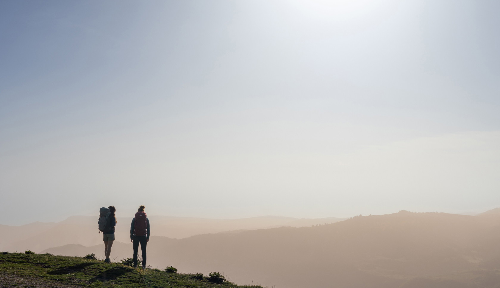 Twee personen met rugzak kijken tijdens golden hour uit over bergen