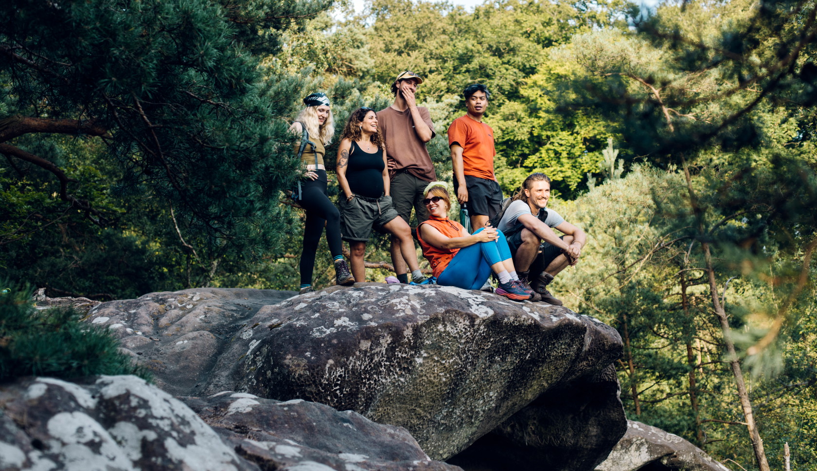 Groep wandelaars staat en zit boven op een grote rots in het bos