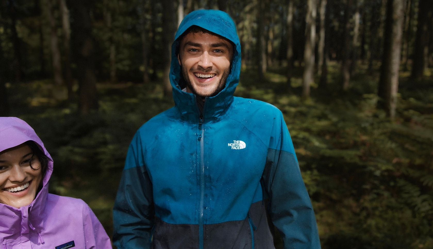 Man in blauwe The North Face-regenjas met capuchon in het bos.