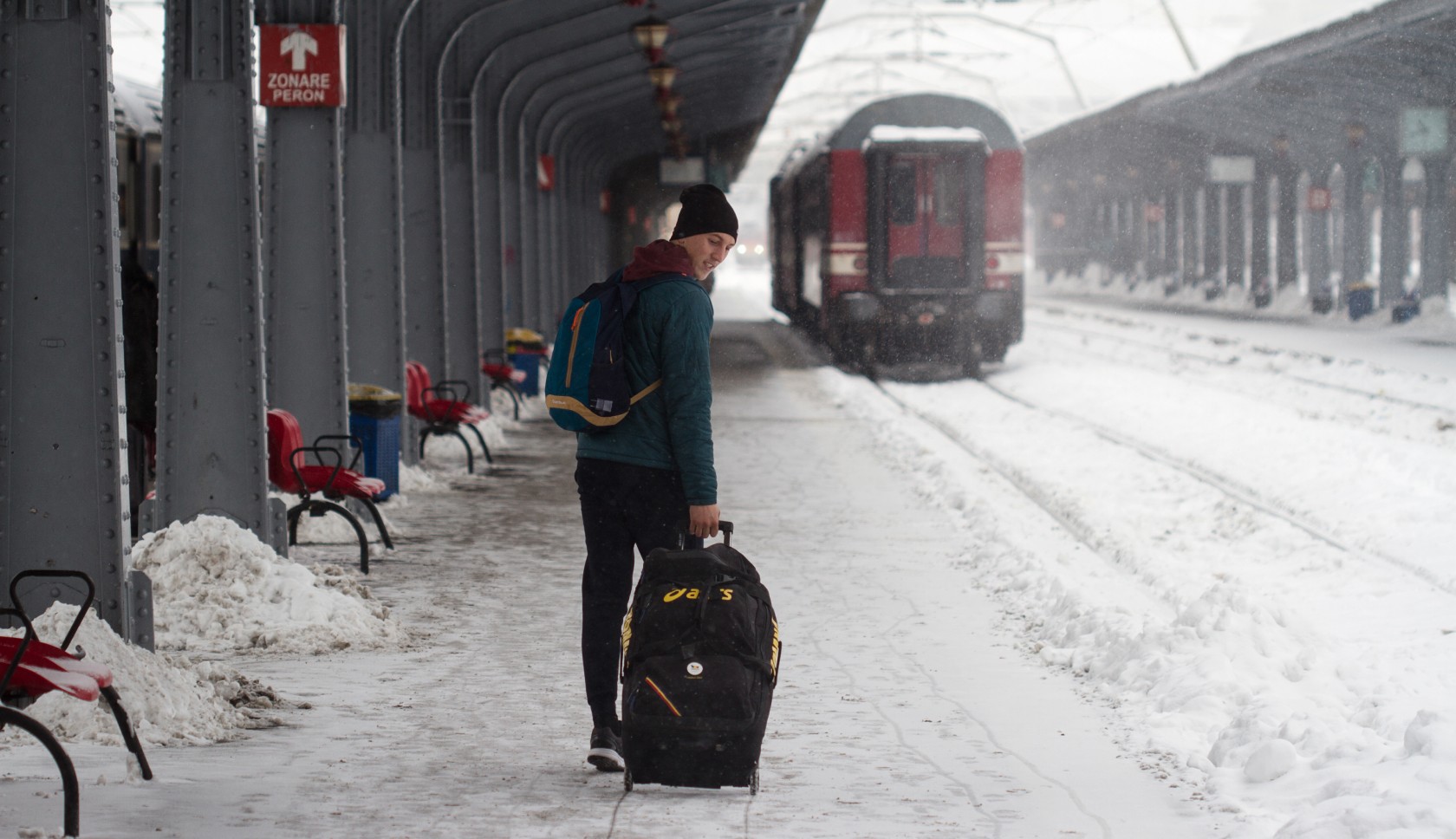 Man staat met een koffer op een besneeuwd perron op de trein te wachten.