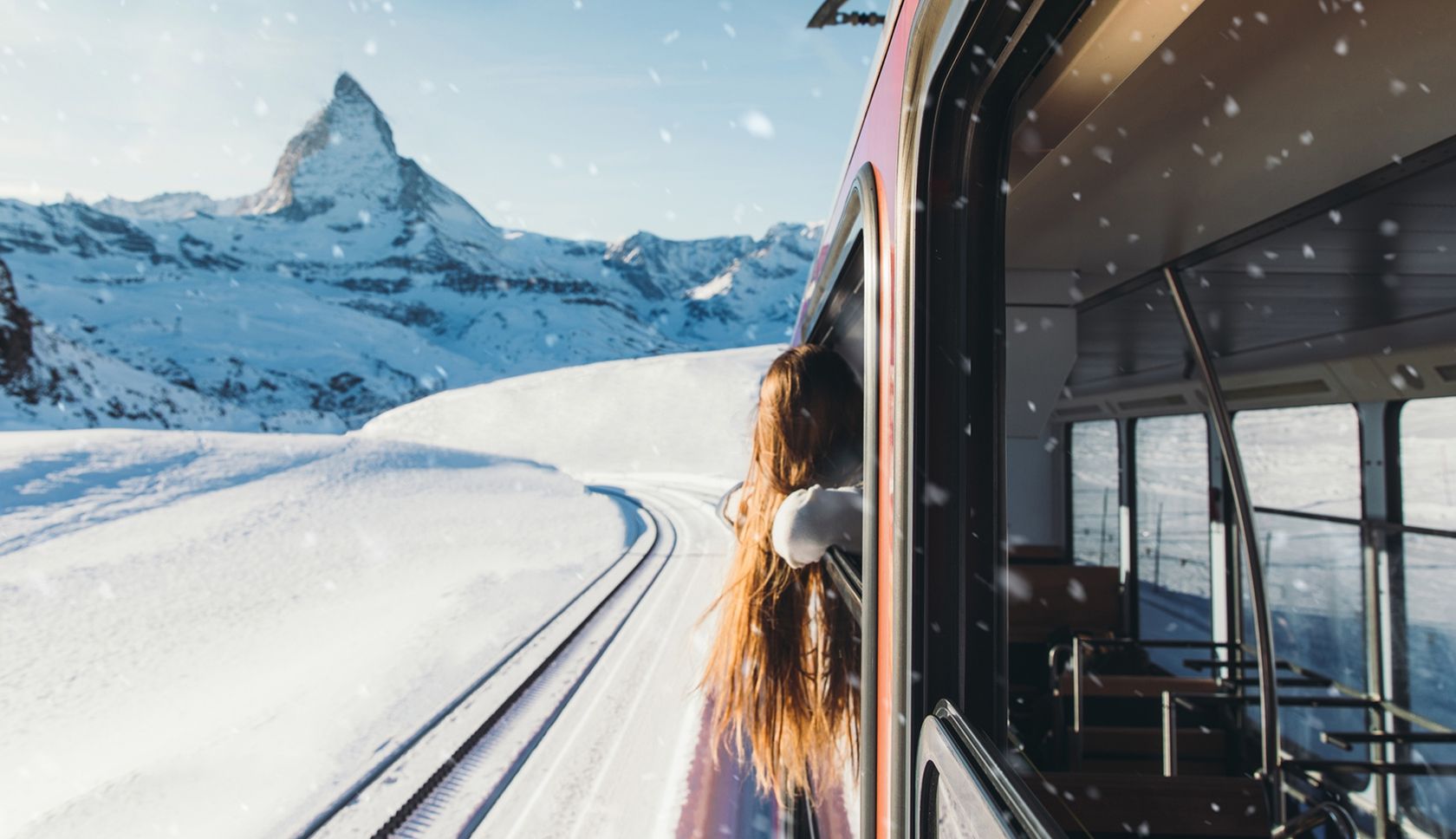 Rood-witte trein rijdt door een besneeuwd berglandschap.