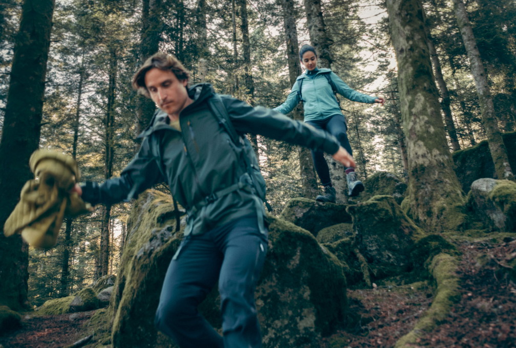 Twee wandelaars in een bos dragen Ayacucho-outdoorkleding tijdens een wandeling over rotsachtig terrein.