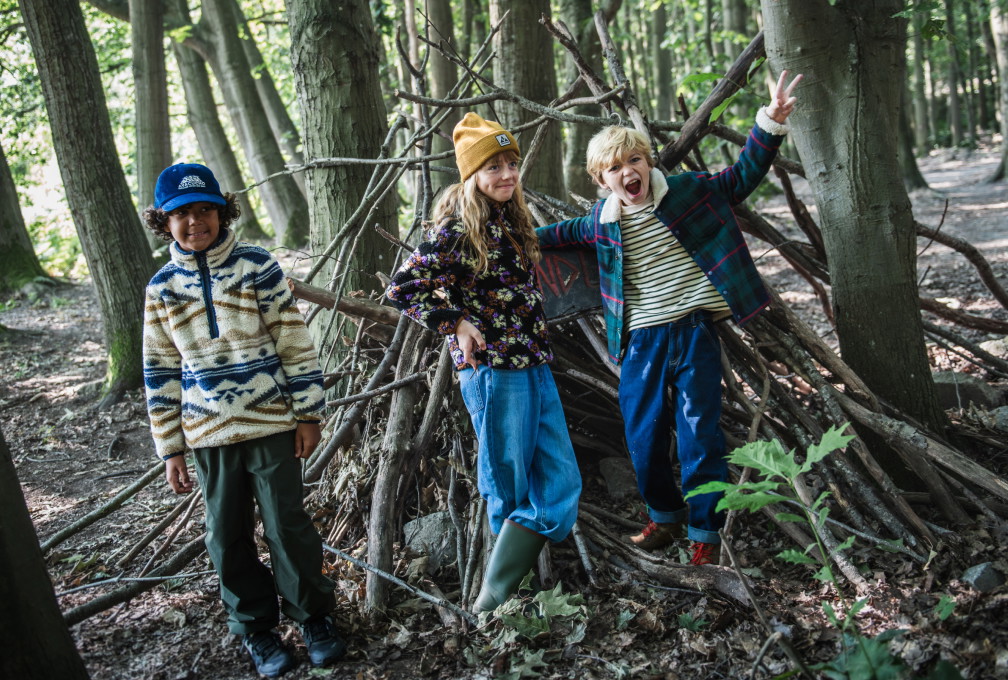 Drie kinderen in kleurrijke Ayacucho-outdoorkleding spelen samen in een bos.
