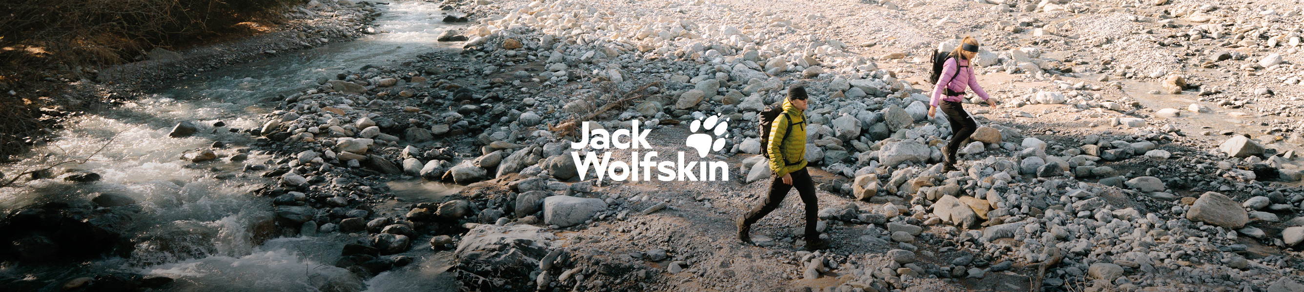 Twee wandelaars met Jack Wolfskin outdoorjassen en rugzakken lopen langs een rotsachtige rivier